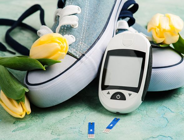 Close up of glucose meter, gumshoes and yellow tulips on blue concerte background